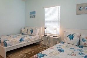 Ein Schlafzimmer mit zwei Betten, jedes mit einer Bettdecke im Meeresschildkröten-Design, einem Fenster mit Jalousien und einem kleinen Tisch mit zwei Lampen.
