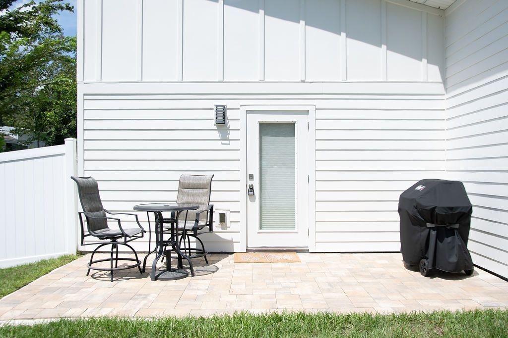 A patio with a table and chairs, a barbecue grill, and a white exterior wall.