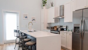 Cocina moderna con armarios blancos, refrigerador de acero inoxidable, una isla central con taburetes de bar y una ventana que proporciona luz natural.