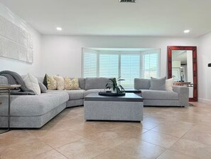 A modern living room with a grey sectional sofa, a coffee table, and a large window with blinds. - Waterfront Oasis - Boat, Pool, Hot Tub & Outdoor Living (Cape Coral)