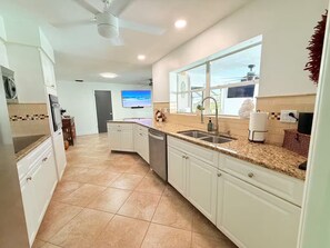 A kitchen with white cabinets, a granite countertop, a window with a view, and a ceiling fan. - Waterfront Oasis - Boat, Pool, Hot Tub & Outdoor Living (Cape Coral)