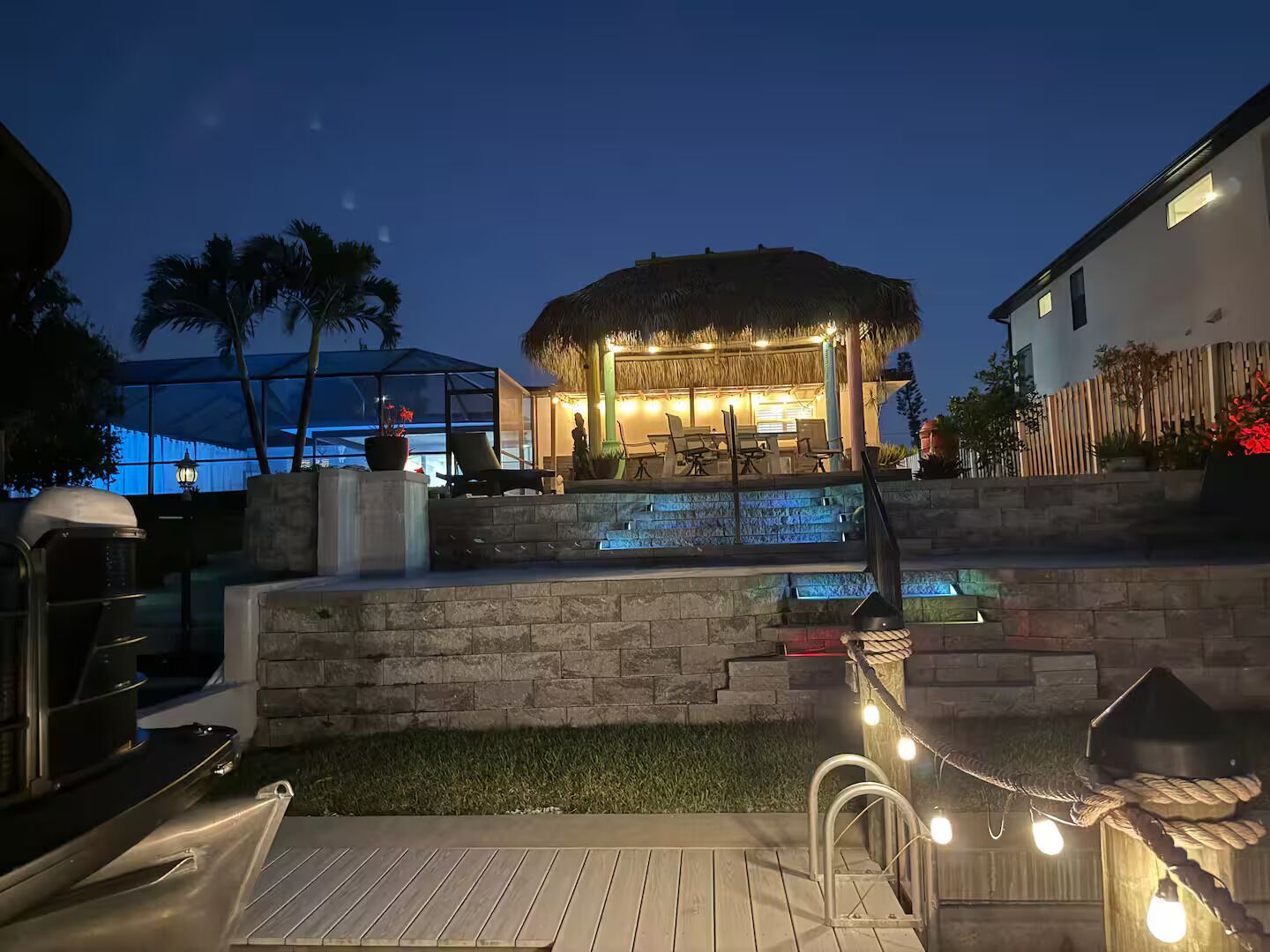 A pool area with a thatched-roof structure, outdoor seating, and a stone wall.