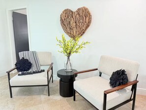 Una habitación con dos sillones, un adorno en forma de corazón y un jarrón con flores amarillas.