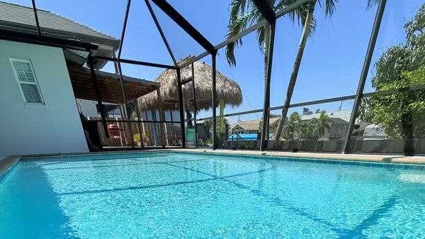 A clear blue swimming pool with a thatched roof structure in the background. - Waterfront Oasis - Boat, Pool, Hot Tub & Outdoor Living (Cape Coral)
