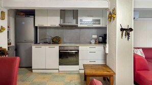 Cocina compacta con refrigerador, microondas, horno y lavamanos. Hay una pequeña mesa de madera y una silla roja en la habitación.