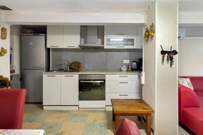 Cocina compacta con refrigerador, microondas, horno y lavamanos. Hay una pequeña mesa de madera y una silla roja en la habitación.