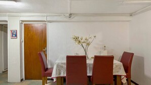 Un comedor con una mesa dispuesta para cuatro, un florero con flores y una puerta a la izquierda.