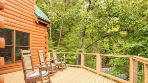 Eine Blockhütte mit einer Veranda, auf der Schaukelstühle stehen, und Blick auf einen Wald.