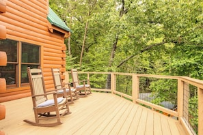 Eine Blockhütte mit einer Veranda, auf der Schaukelstühle stehen, und Blick auf einen Wald.
