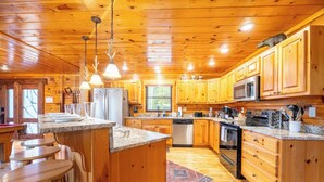 Ein Interieur einer Holzhütte mit einer Küche, die sich durch Granit Arbeitsplatten, Holzschränke, einen Kühlschrank, eine Mikrowelle, einen Herd und Barhocker auszeichnet.