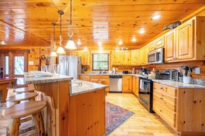 Ein Interieur einer Holzhütte mit einer Küche, die sich durch Granit Arbeitsplatten, Holzschränke, einen Kühlschrank, eine Mikrowelle, einen Herd und Barhocker auszeichnet.