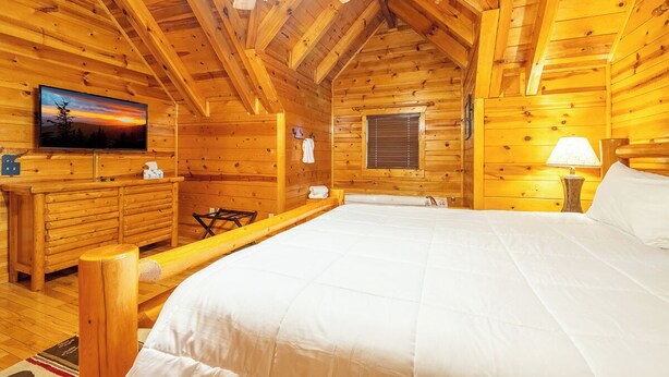 Ein Zimmer in einer Holzhütte mit einem Bett, einem Fernseher, einer Holzkommode und einem Deckenventilator.