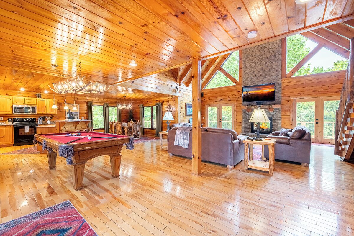 A spacious log cabin interior with a pool table, sofas, and a fireplace.