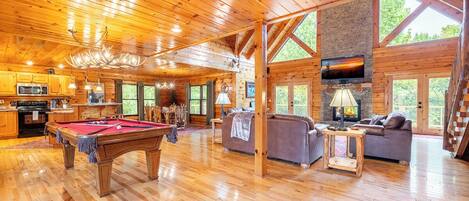 A spacious log cabin interior with a pool table, sofas, and a fireplace.