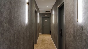 Un pasillo con piso alfombrado, paredes con paneles texturizados y puertas con letreros iluminados.