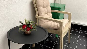 A room with a black tiled floor, a beige armchair, a small round table with a flower vase, and a green storage unit.