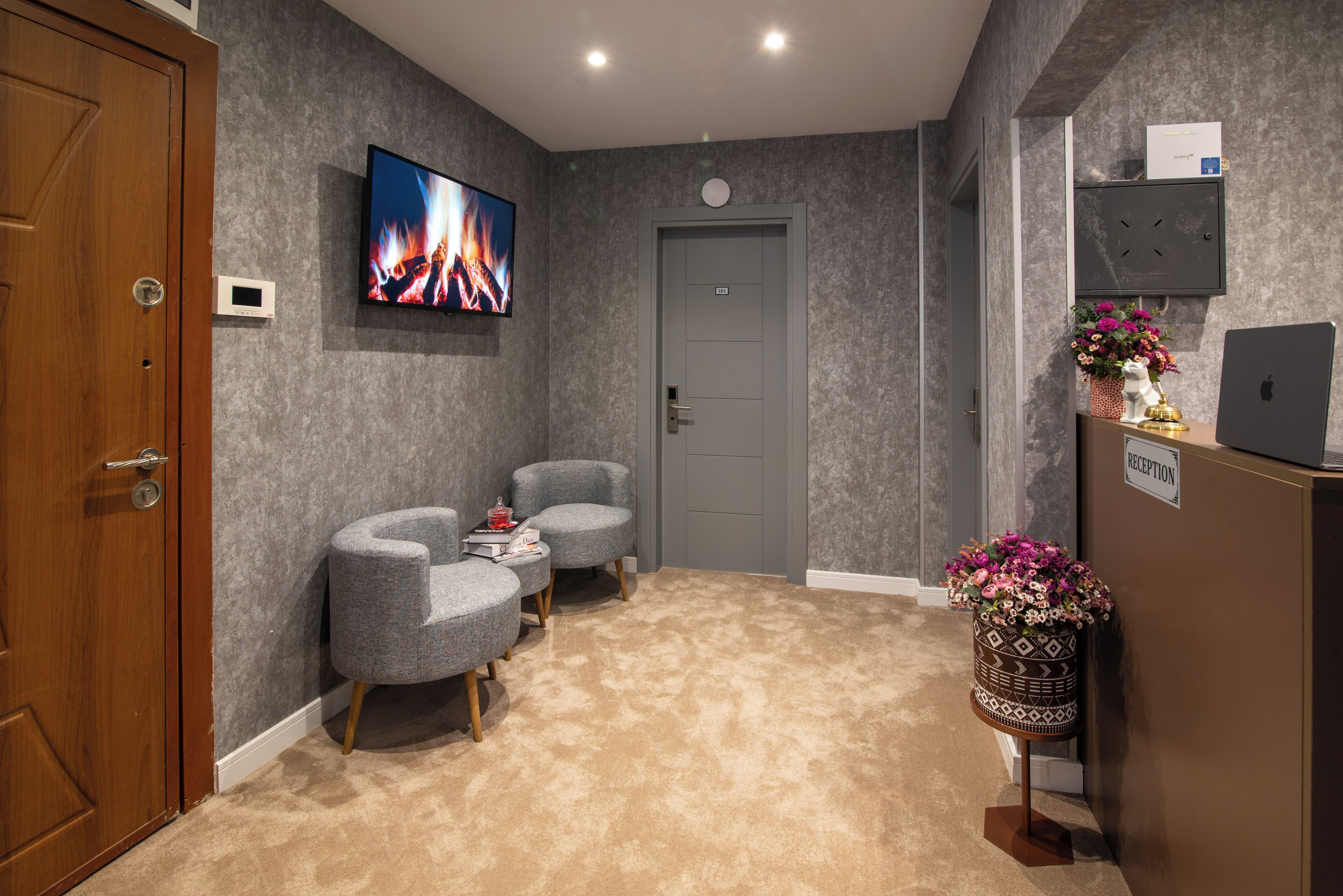 A reception area with a flat-screen TV, two grey armchairs, a reception desk, and a carpeted floor.