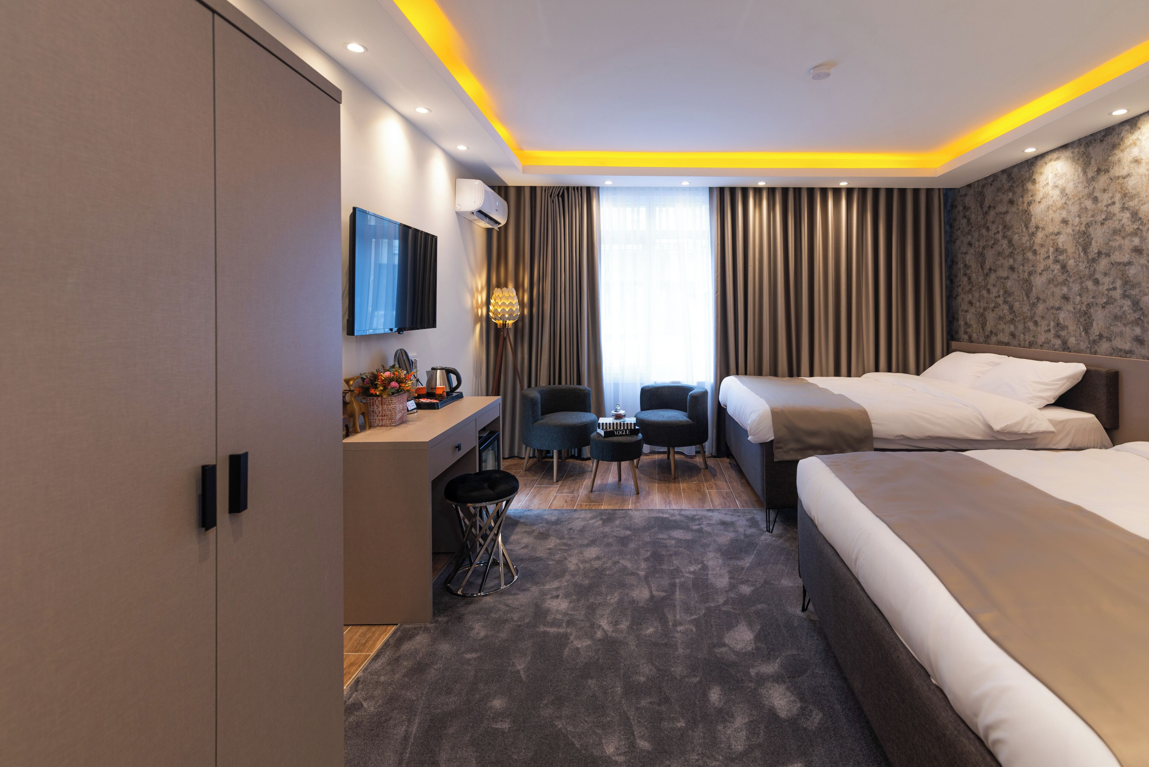 Una habitación de hotel moderna con cama, escritorio, silla, televisor y ventana con cortinas.