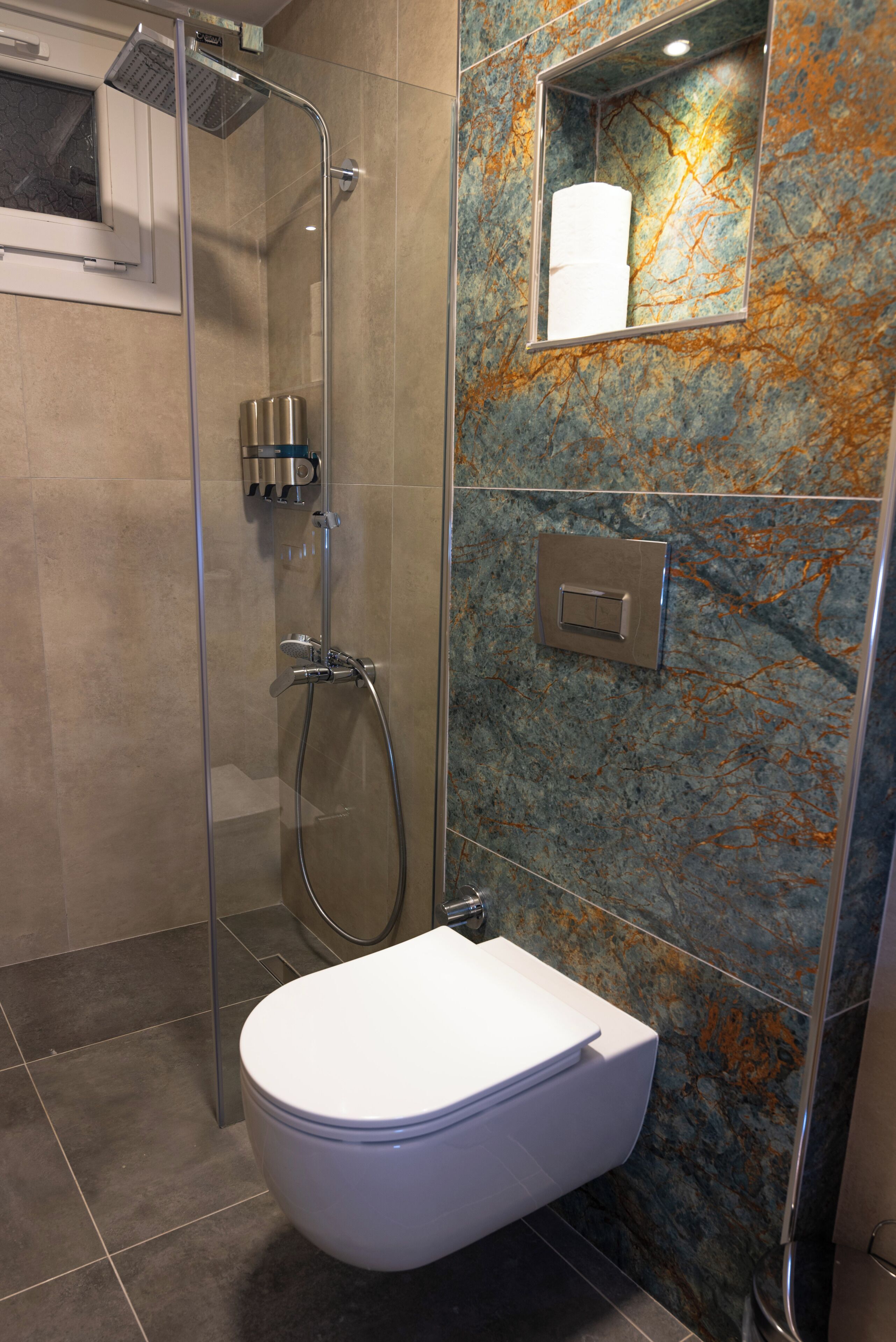 Un baño moderno con ducha de vidrio, inodoro y pared de mármol.