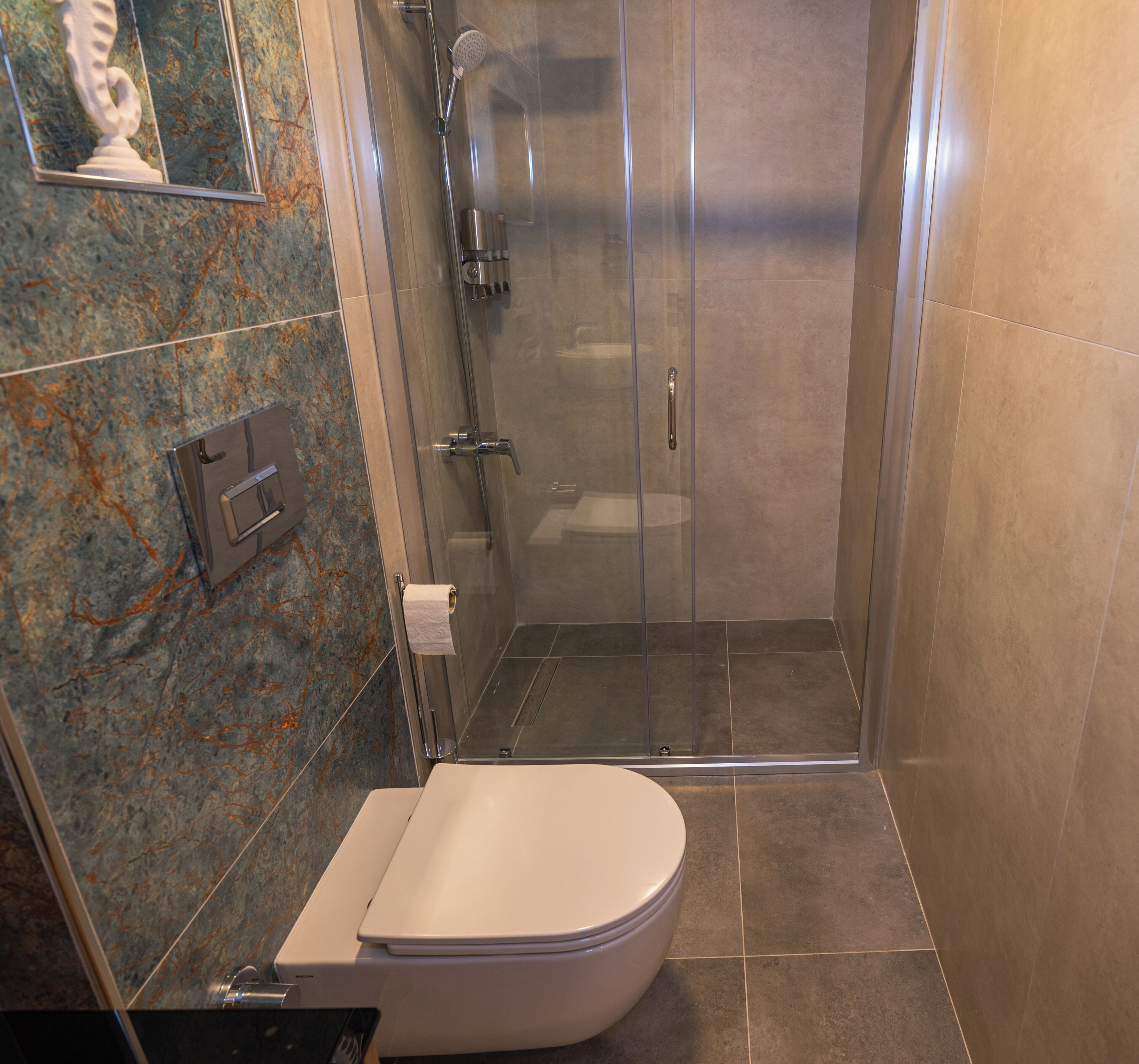A bathroom with a toilet, shower, and marble-tiled walls.