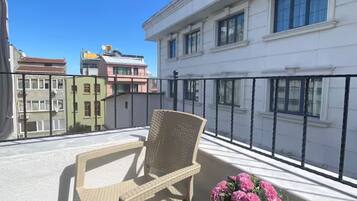 Un balcon avec une chaise en osier et une table, un pot de fleurs et une vue sur les immebles.