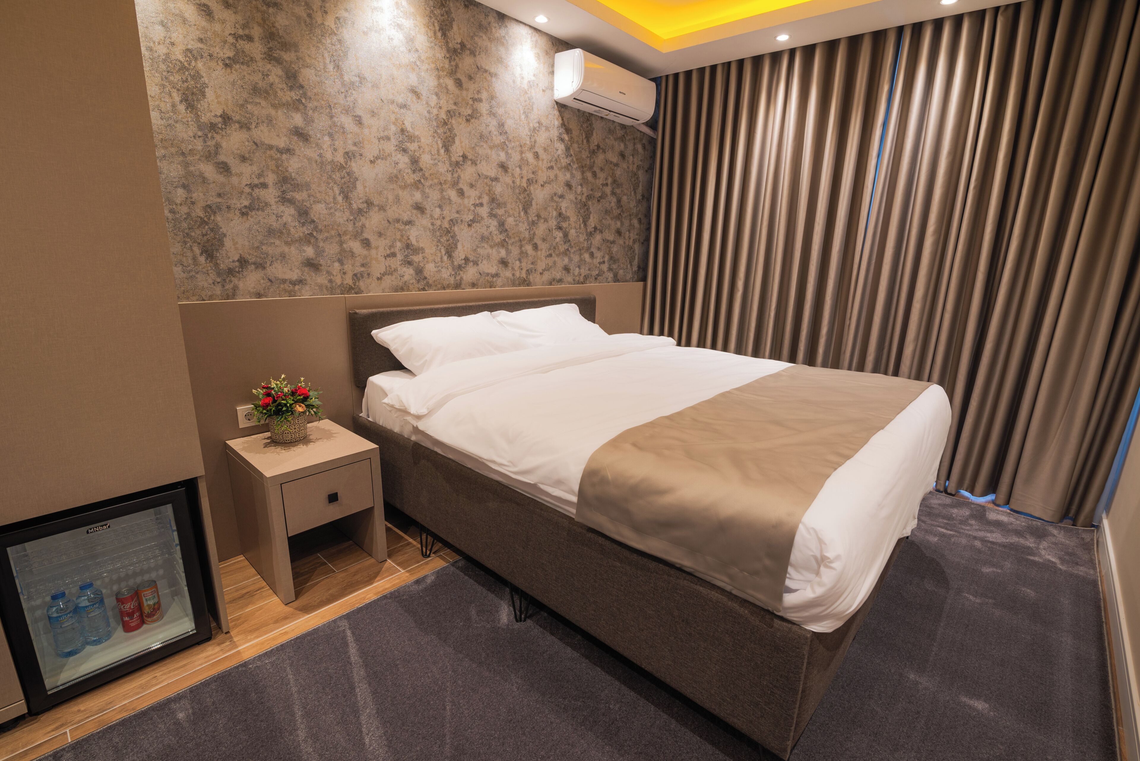 Een hotelkamer met een bed, nachtkastje, televisie en gordijn.