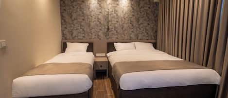 A hotel room with two beds, a wooden floor, a textured wall, and a curtain on the right.