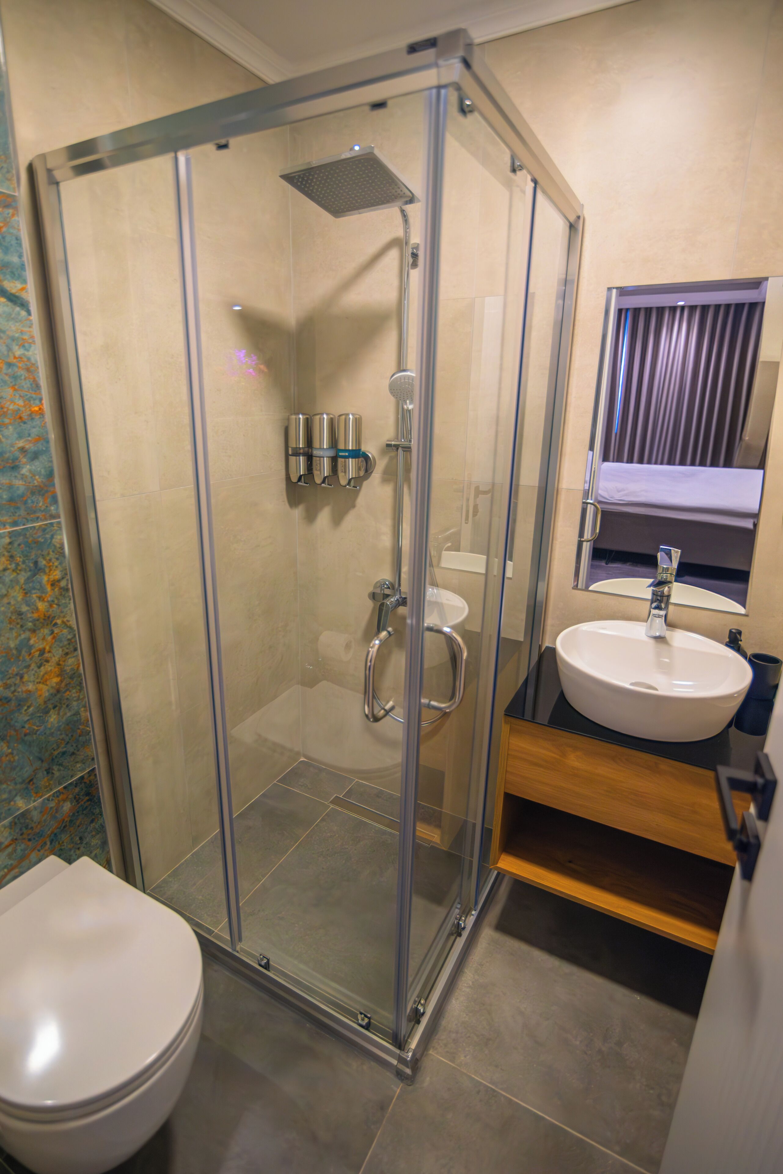A glass-enclosed shower stall with a handheld showerhead, a toilet, and a sink with a mirror above it.