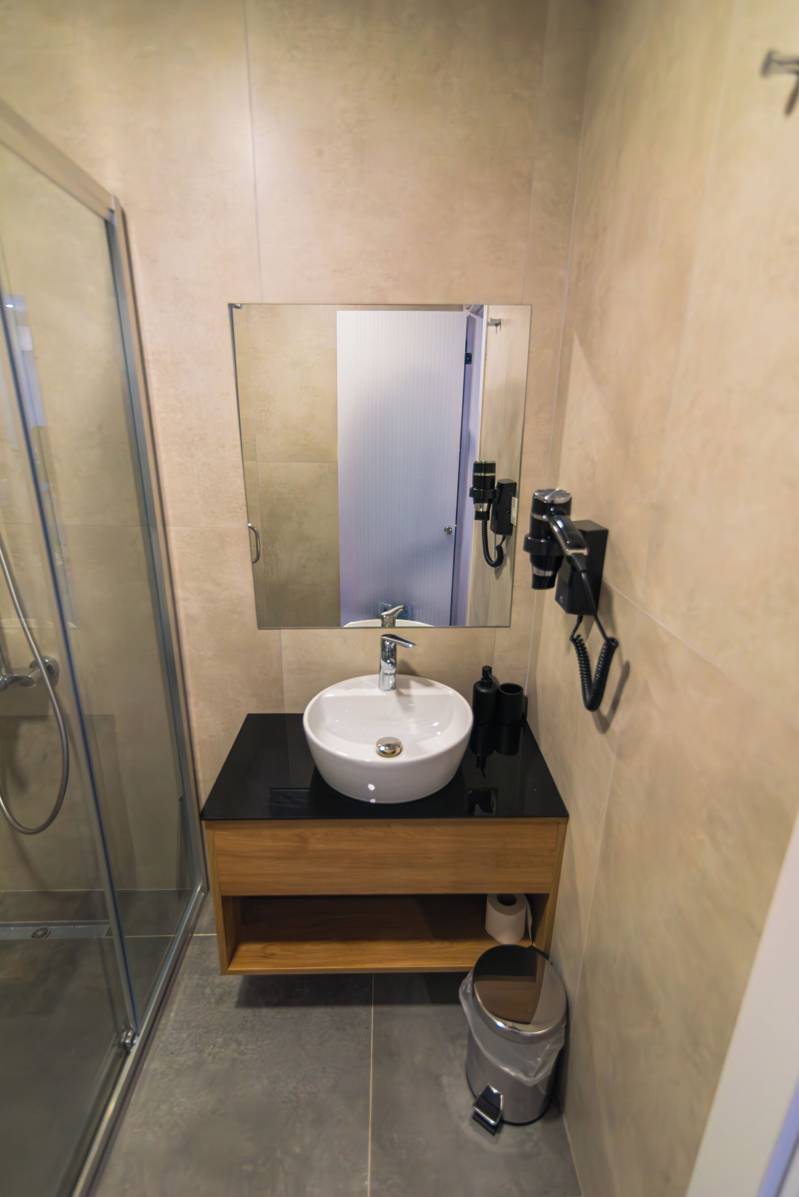 A bathroom with a glass shower enclosure, a sink with a mirror above it, and a toilet paper holder on the wall.