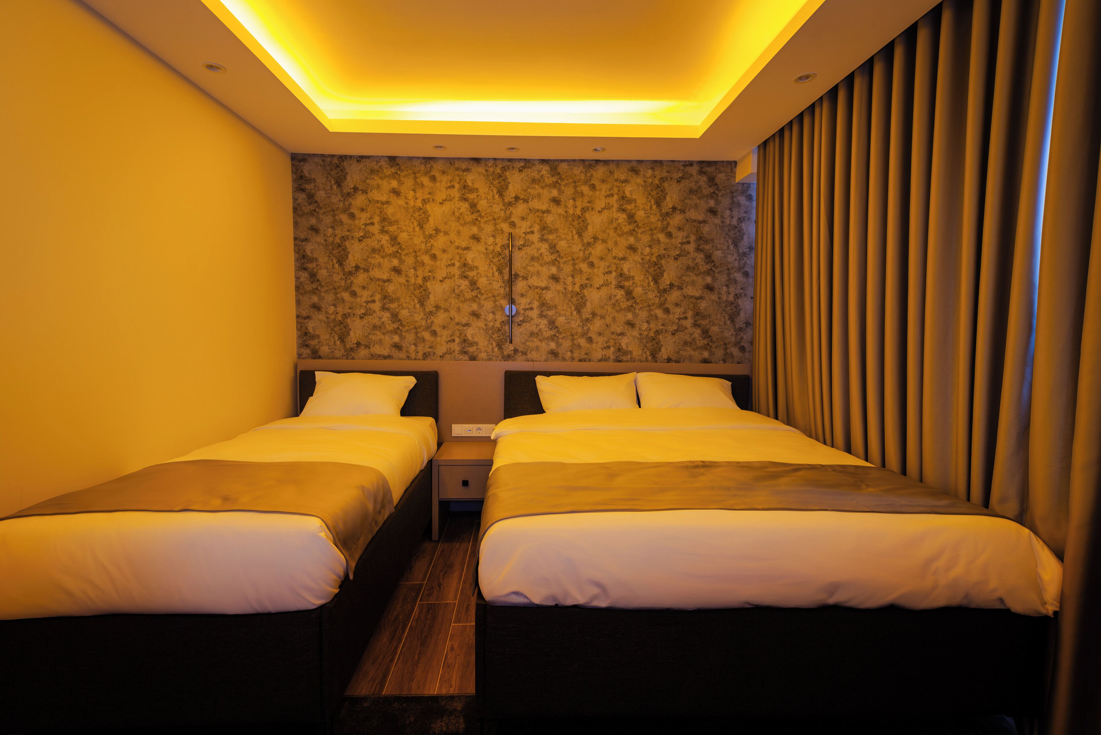 A hotel room with two beds, a nightstand, and a wall with a textured pattern.
