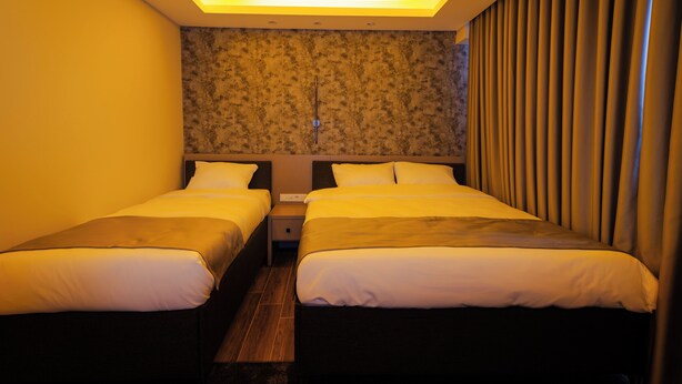 Habitación de hotel con dos camas, una mesita de noche y una pared con textura.