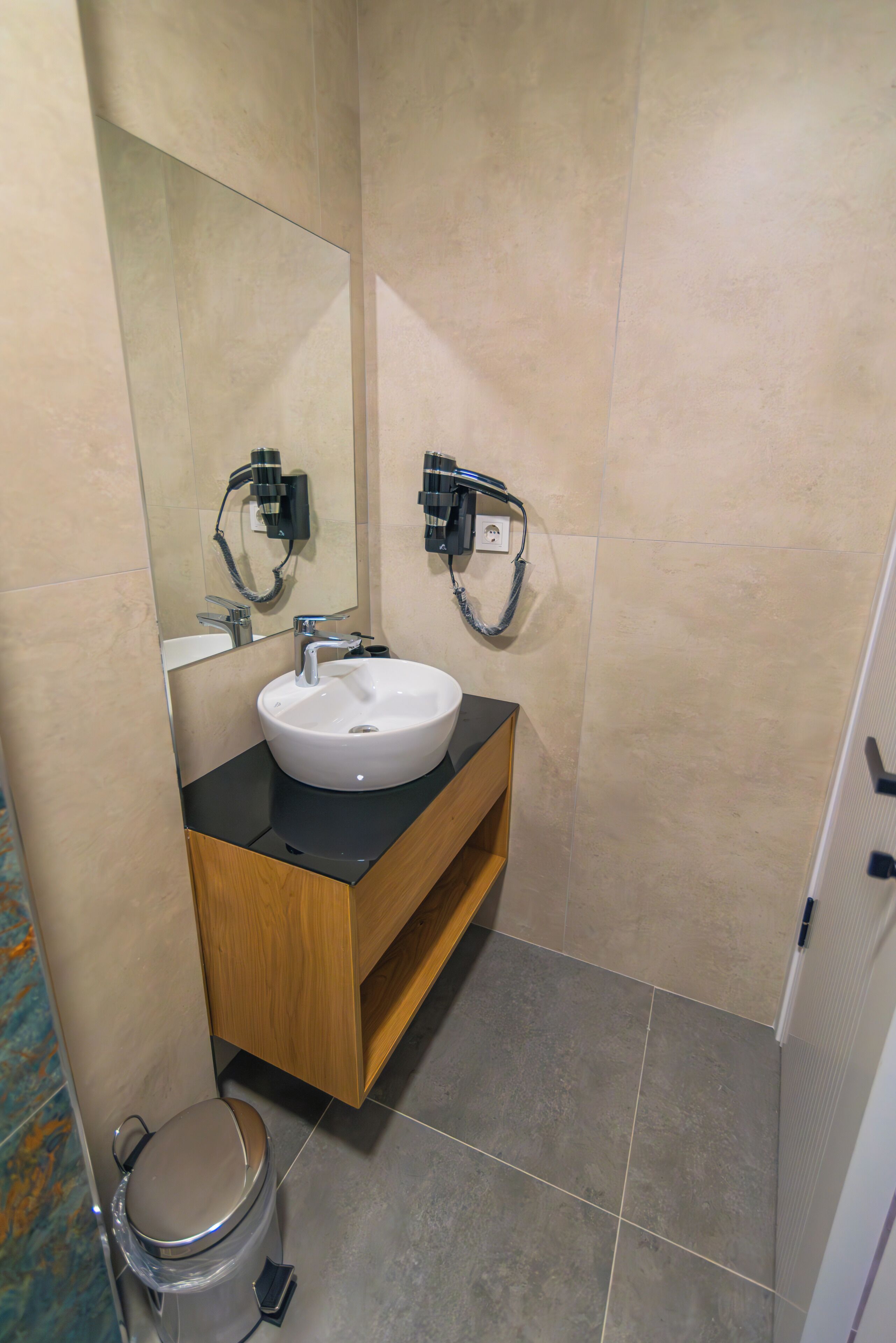 Een moderne badkamer met een wit wasbakje, een houten wastafelmeubel en een spiegel.