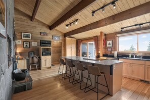 A spacious kitchen with wooden beams, a large island with bar stools, and a view through the window.