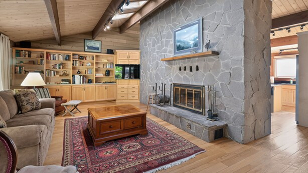 A spacious living room with a stone fireplace, wooden bookshelves, a comfortable sofa, and a large rug. - Columbia Gorge - Mosier Bluff | River Views & Pool (Mosier)