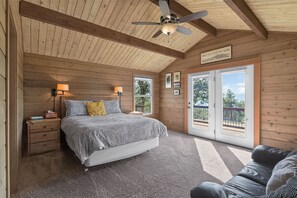 Ein Schlafzimmer mit einem Bett, Nachttischlampen, einem Deckenventilator und Blick durch eine Glastür.