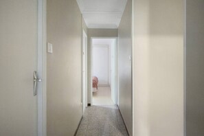 A narrow hallway with a door on the left and a room visible at the end.