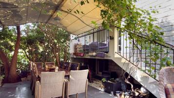 Un patio exterior con mobiliario de mimbre, una zona de estar cubierta y una escalera que conduce a un nivel superior.