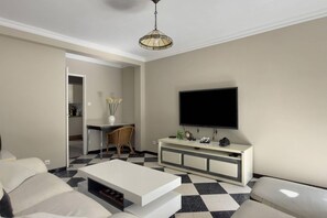 Un salon moderne avec un téléviseur à écran plat, un canapé blanc, une table basse et un sol à carreaux.