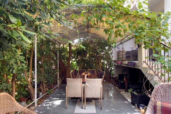 An outdoor dining area with a pergola, wicker furniture, and a view of a building with a balcony.