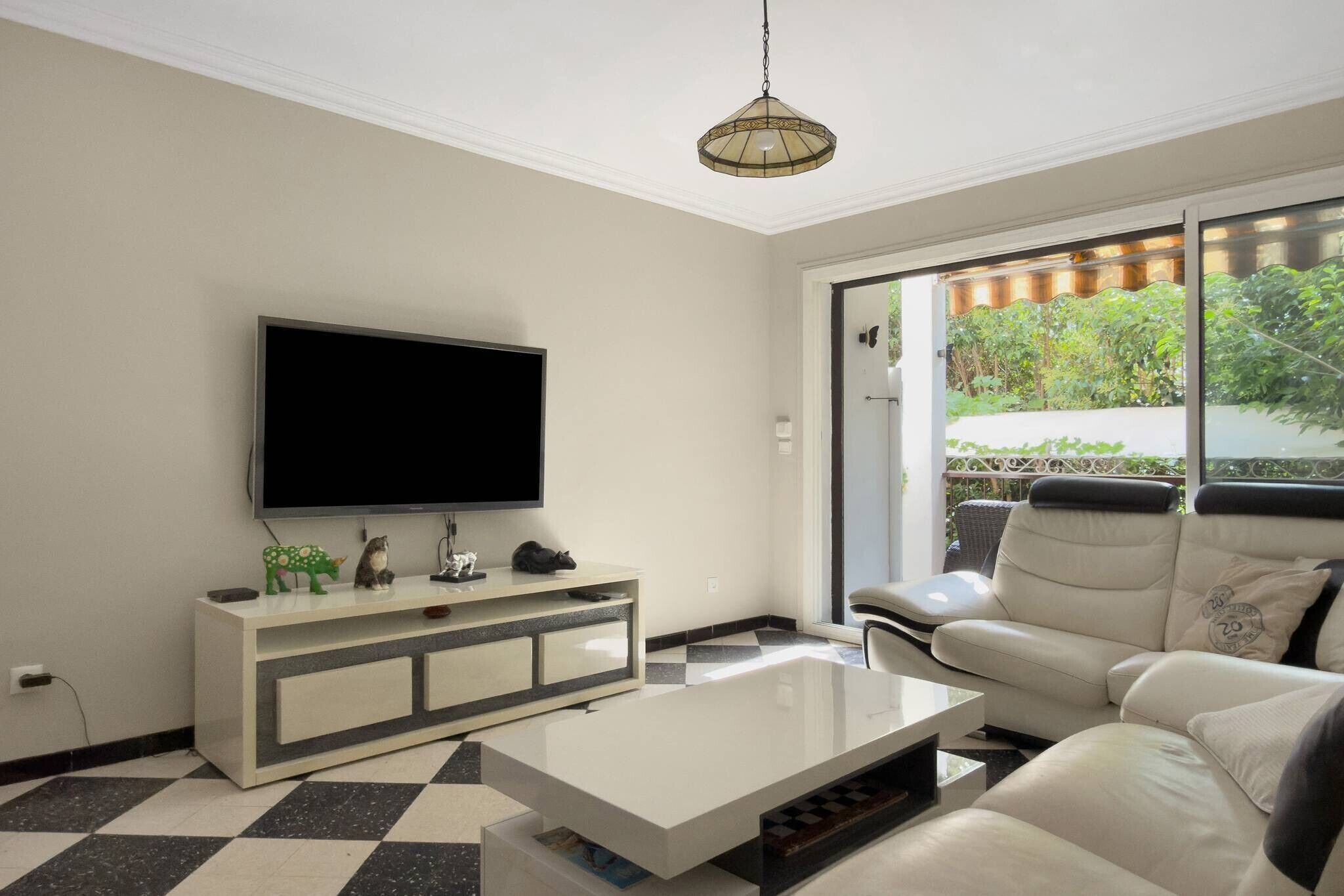 Un salon moderne doté d’un téléviseur à écran plat, d’une console blanche, d’un canapé en cuir et d’une grande fenêtre donnant sur un paysage verdoyant.