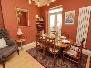 A dining area with a round table, chairs, a lamp, a bookshelf, and a window with a view.