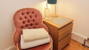 A tufted chair with a cushion, a bedside table with a lamp, and a bottle. - 18 Kent Street (Cardiff)