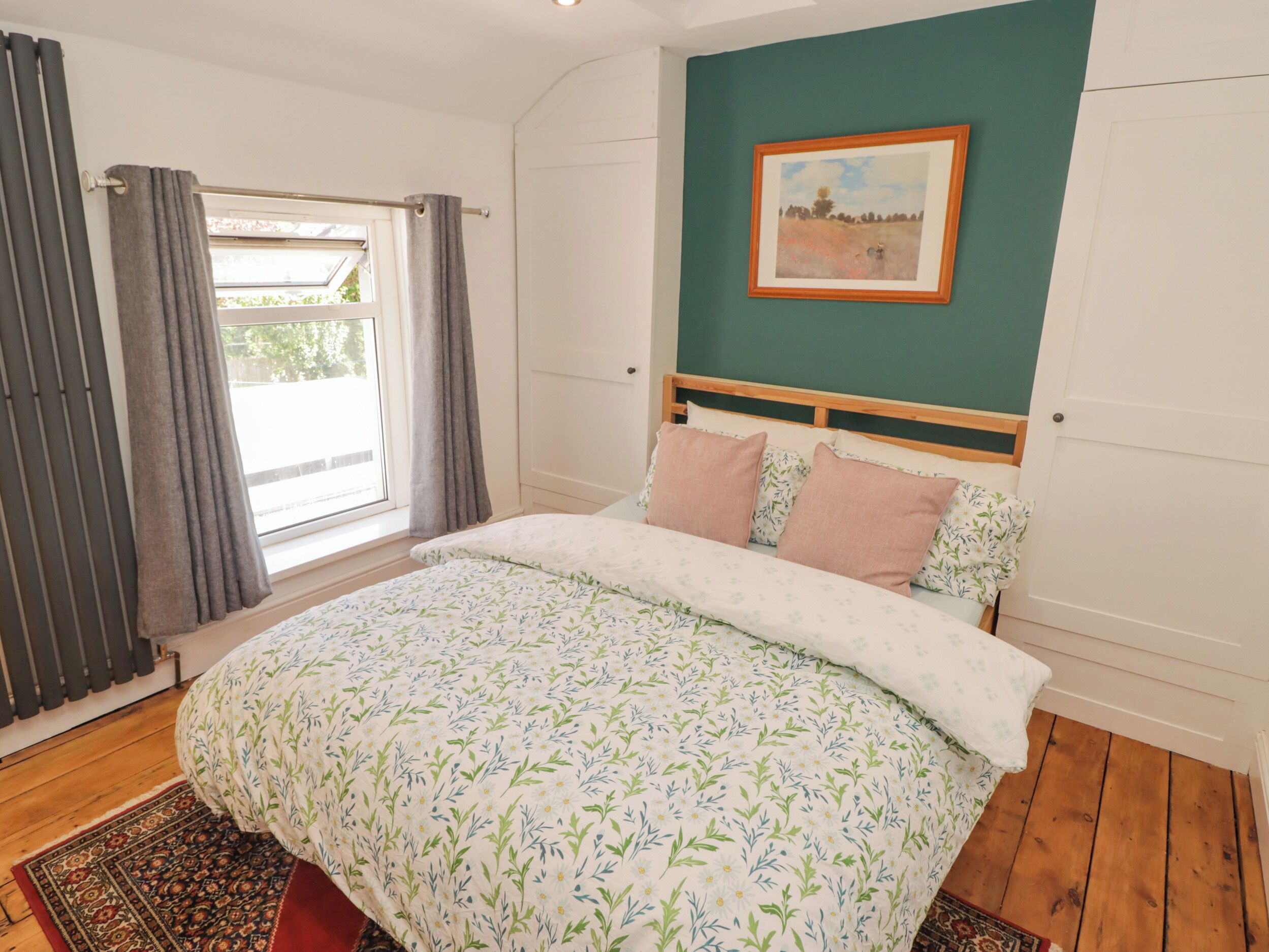 A bedroom with a bed, a window with curtains, a painting on the wall, and a patterned rug.