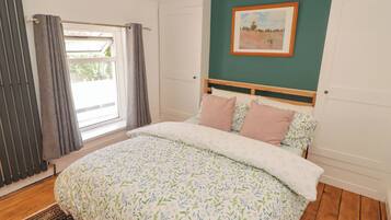 A bedroom with a bed, a window with curtains, a painting on the wall, and a patterned rug.