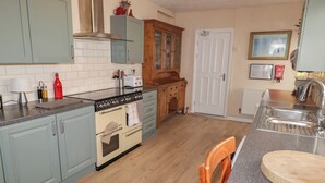 Una cocina con armarios azul claro, una estufa blanca, un mueble de madera con puertas de cristal, una puerta blanca y una silla de madera.