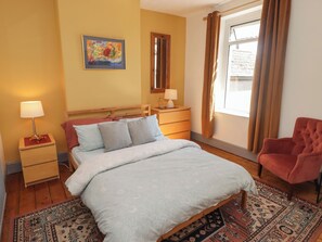 A bedroom with a bed, bedside tables, a chair, a window with curtains, and a painting on the wall.