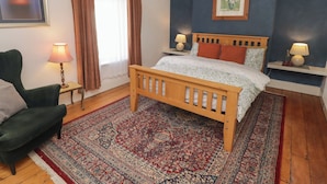 A bedroom with a wooden bed, a green armchair, a patterned rug, and a blue accent wall. - 18 Kent Street (Cardiff)