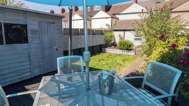A patio with a table and chairs, a blue umbrella, and a garden with plants and flowers. - 18 Kent Street (Cardiff)