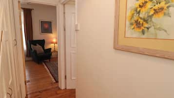 A hallway with wooden flooring leading to a room with a green armchair and a lamp.