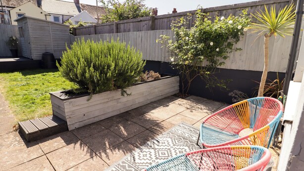 Un patio con un jardín elevado, dos sillas coloridas y una alfombra estampada.